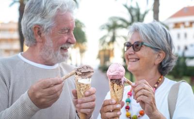 Two grey hair adults smile at each other holding dripping ice cream cones